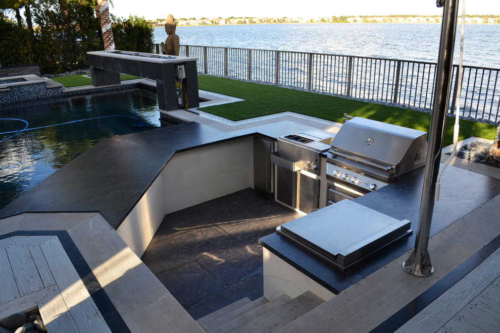 Aménagement d'une très grande terrasse arrière moderne avec une cuisine d'été et des pavés en pierre naturelle.