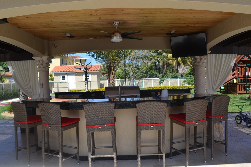Expansive modern back patio in Miami with an outdoor kitchen, natural stone paving and a gazebo.