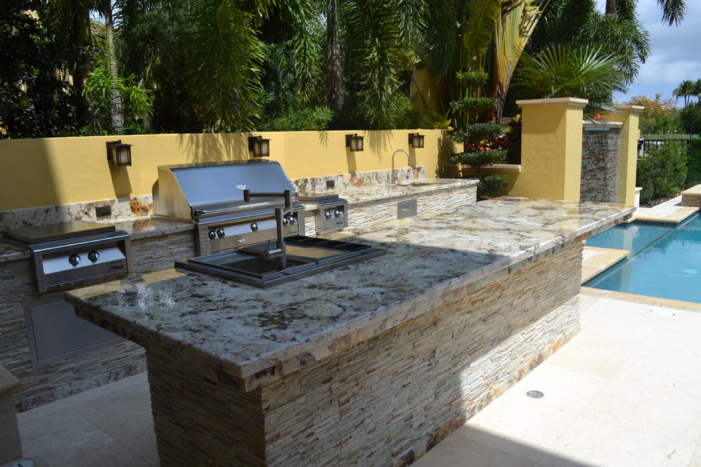 Patio kitchen - huge traditional backyard stone patio kitchen idea in Miami with a pergola