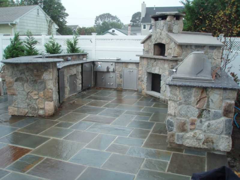 Réalisation d'une grande terrasse arrière tradition avec une cuisine d'été, des pavés en pierre naturelle et aucune couverture.