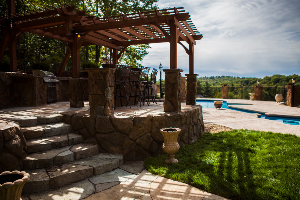 Réalisation d'une grande terrasse arrière chalet avec une cuisine d'été, des pavés en pierre naturelle et une pergola.