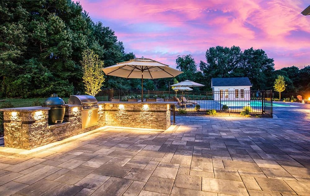 Cette photo montre une terrasse arrière moderne avec une cuisine d'été, des pavés en pierre naturelle et un auvent.