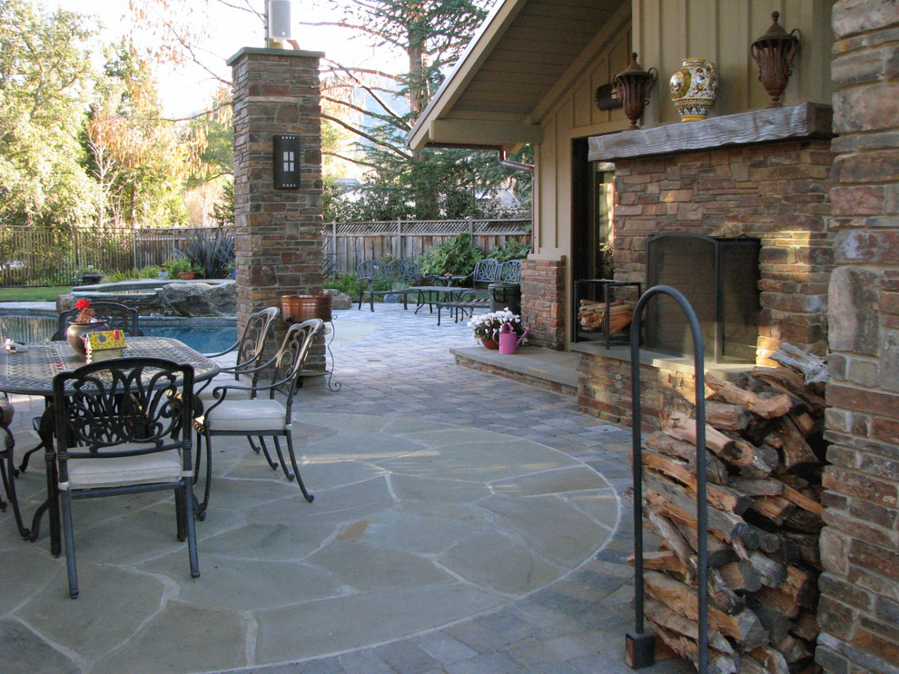 Immagine di un ampio patio o portico country dietro casa con un focolare, pavimentazioni in pietra naturale e una pergola