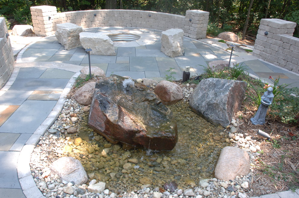 This is an example of a back patio in Other with a water feature, natural stone paving and no cover.