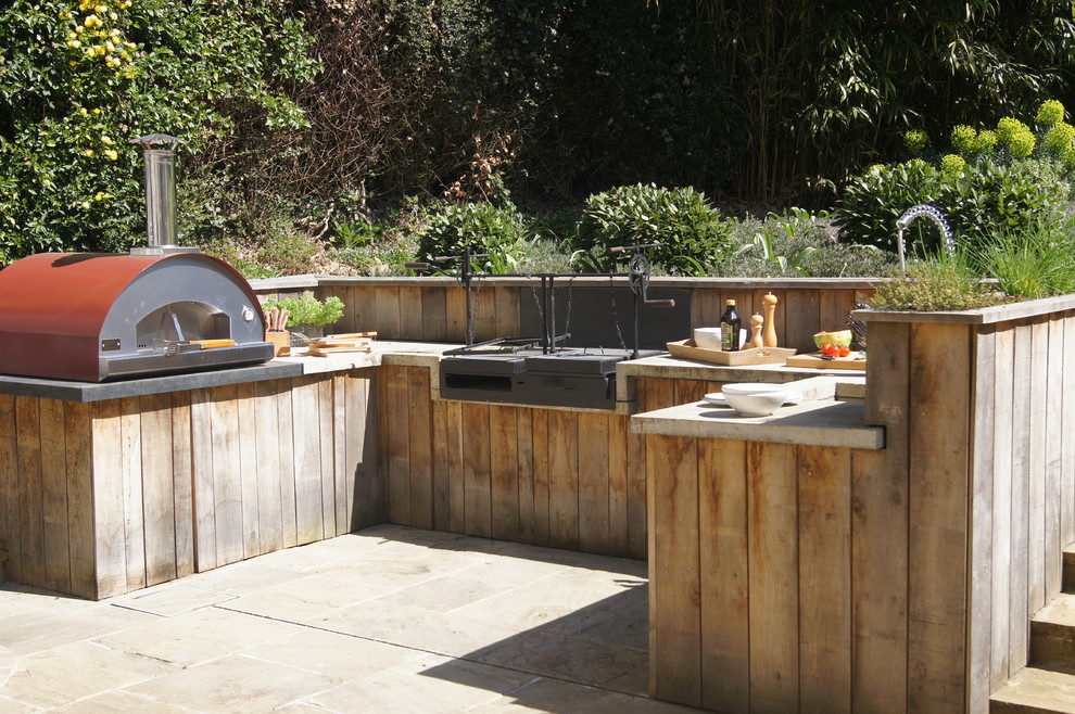 Cette photo montre une grande terrasse arrière nature avec une cuisine d'été, des pavés en pierre naturelle et une pergola.