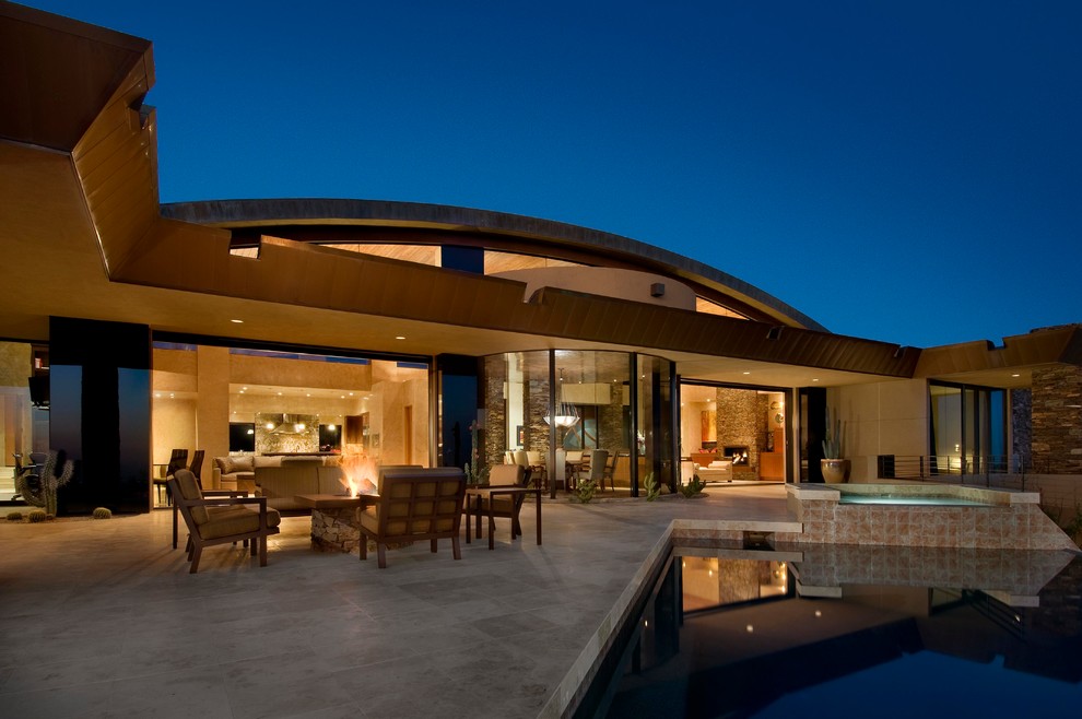 Réalisation d'une grande terrasse arrière minimaliste avec un foyer extérieur, du carrelage et une extension de toiture.