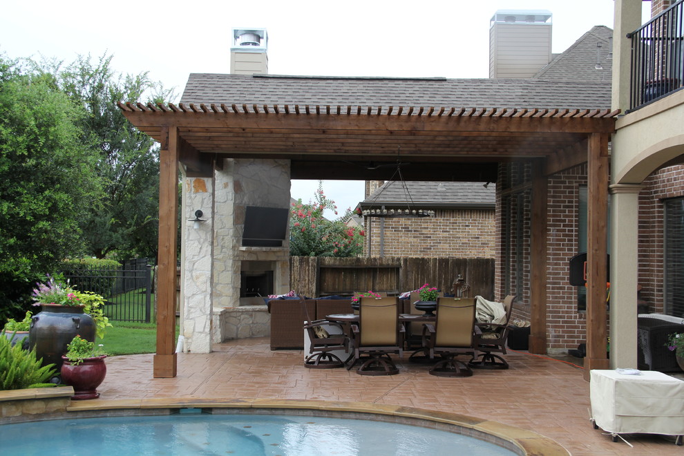 Photo of a large traditional back patio in Houston with a fire feature, stamped concrete and a roof extension.