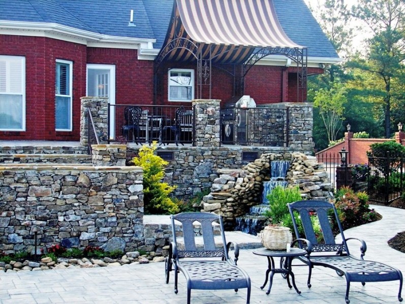 Imagen de patio contemporáneo de tamaño medio en patio trasero con fuente, adoquines de ladrillo y toldo