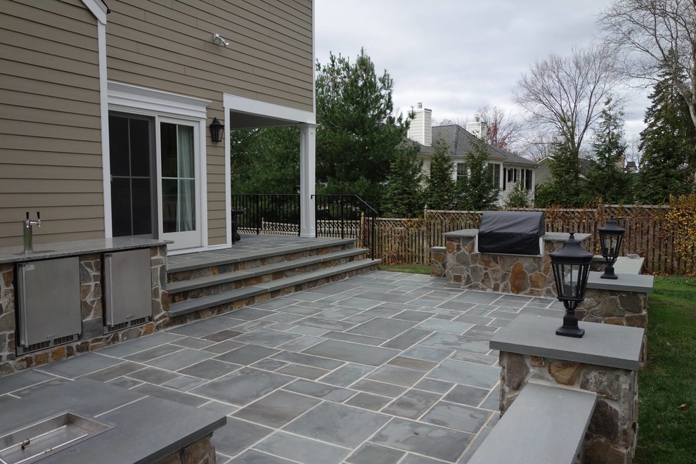 Cette image montre une grande terrasse arrière traditionnelle avec une cuisine d'été et des pavés en pierre naturelle.