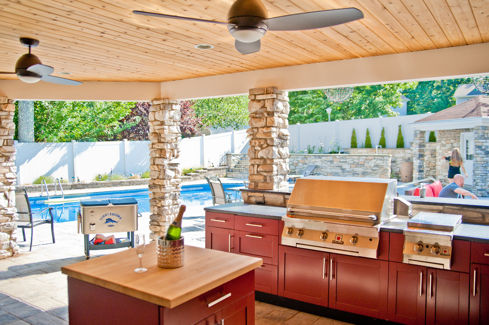 На фото: большой двор на заднем дворе в современном стиле с покрытием из каменной брусчатки, летней кухней и навесом
