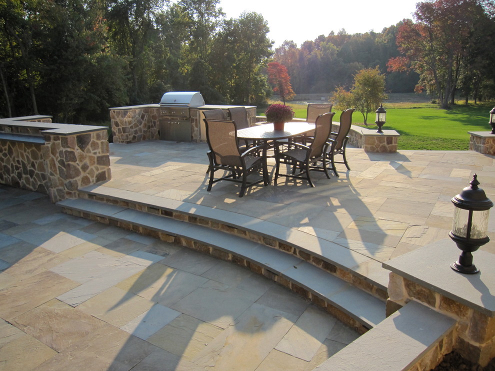 Example of a huge classic backyard stone patio kitchen design in Philadelphia with no cover