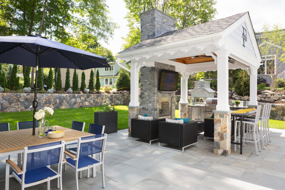 Cette photo montre une grande terrasse arrière chic avec une cuisine d'été, des pavés en pierre naturelle et un gazebo ou pavillon.
