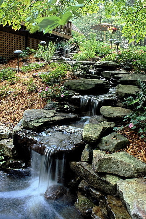 Imagen de jardín clásico de tamaño medio en patio trasero con fuente y adoquines de piedra natural