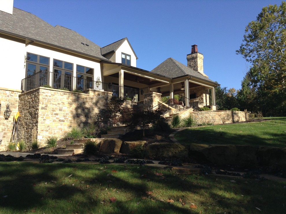 Réalisation d'une grande terrasse arrière tradition avec un foyer extérieur et des pavés en pierre naturelle.
