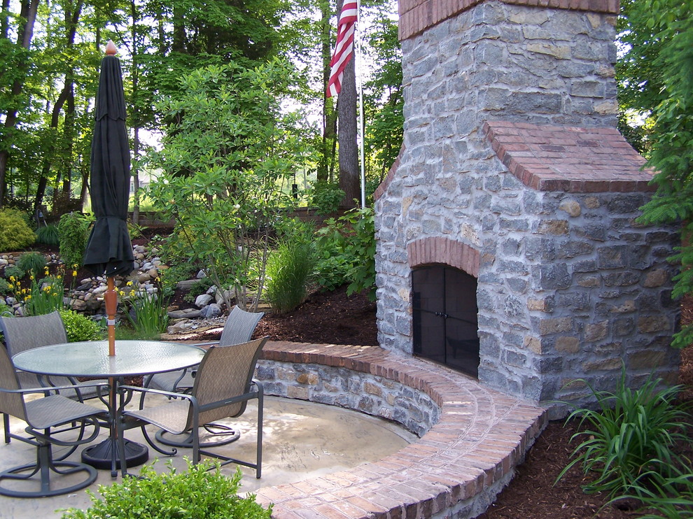 Inspiration pour une grande terrasse arrière traditionnelle avec un foyer extérieur et des pavés en pierre naturelle.