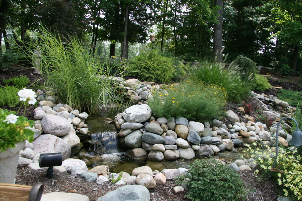 Imagen de jardín clásico grande en patio trasero con fuente y adoquines de piedra natural