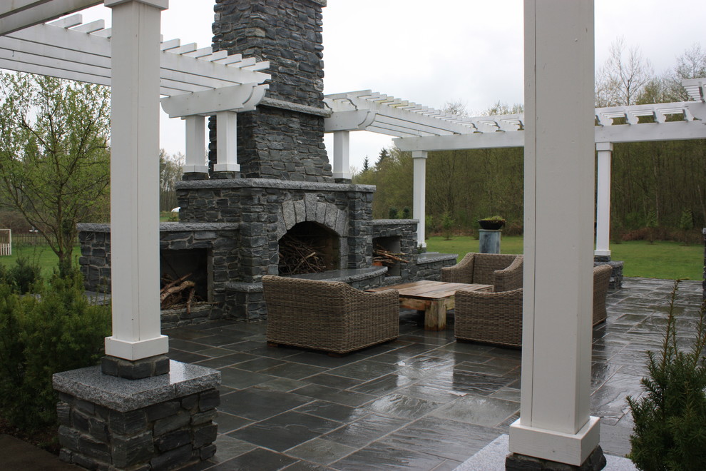 Réalisation d'une grande terrasse tradition avec un foyer extérieur, une cour, des pavés en pierre naturelle et une pergola.