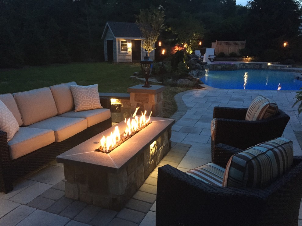 This is an example of a large traditional back patio in New York with a fire feature, no cover and natural stone paving.