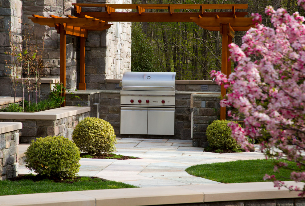 Cette image montre une très grande terrasse latérale traditionnelle avec une cuisine d'été, des pavés en pierre naturelle et une pergola.