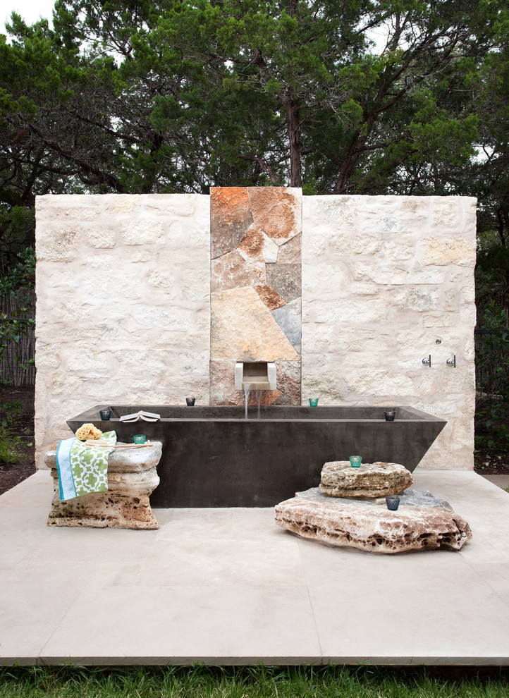 This is an example of a contemporary side patio in Austin with a water feature, natural stone paving and no cover.