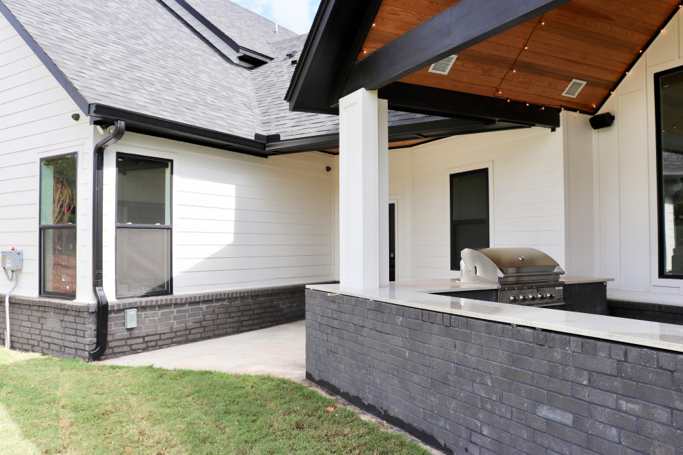 Cette image montre une grande terrasse arrière minimaliste avec une cuisine d'été, une dalle de béton et une extension de toiture.