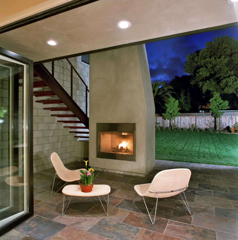Réalisation d'une terrasse arrière design avec un foyer extérieur.