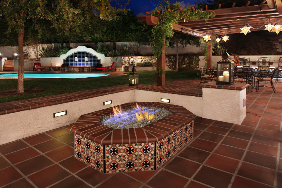 Foto di un grande patio o portico mediterraneo dietro casa con un focolare, piastrelle e una pergola