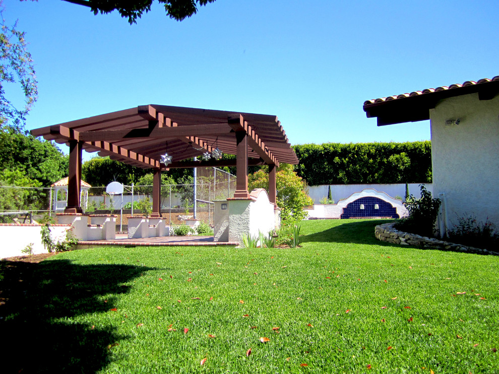 Idee per un grande patio o portico mediterraneo dietro casa con piastrelle e una pergola