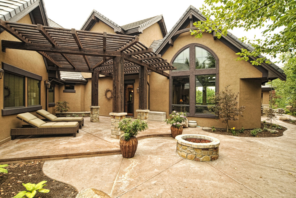 Cette image montre une grande terrasse arrière craftsman avec un foyer extérieur, du béton estampé et une pergola.