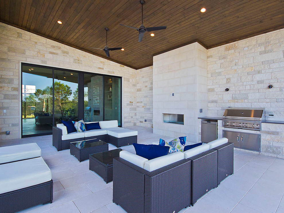 Réalisation d'une très grande terrasse arrière design avec une cuisine d'été, des pavés en pierre naturelle et une extension de toiture.
