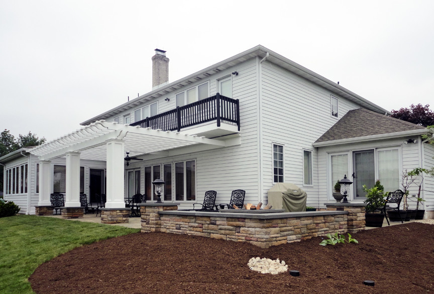 Aménagement d'une grande terrasse arrière classique avec un foyer extérieur, des pavés en pierre naturelle et une pergola.