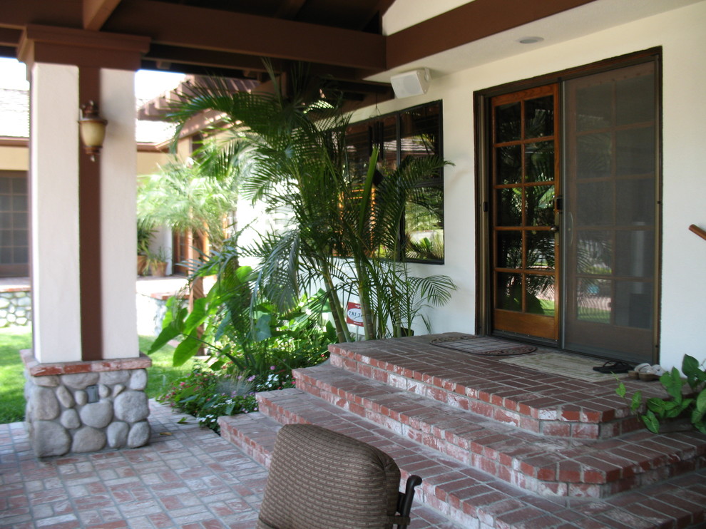 Immagine di un patio o portico chic di medie dimensioni e dietro casa con pavimentazioni in mattoni e un tetto a sbalzo