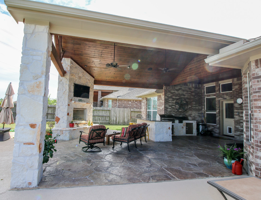 This is an example of a large traditional back patio in Houston with an outdoor kitchen, stamped concrete and a roof extension.