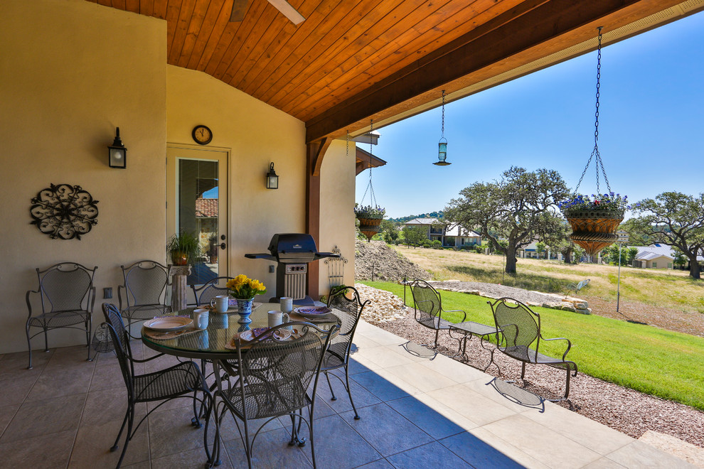 This is an example of a large traditional back patio in Austin with an outdoor kitchen, tiled flooring and a roof extension.