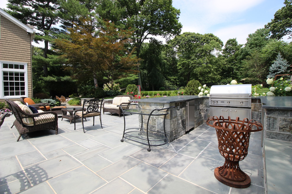 This is an example of an expansive classic back patio in New York with an outdoor kitchen, natural stone paving and no cover.