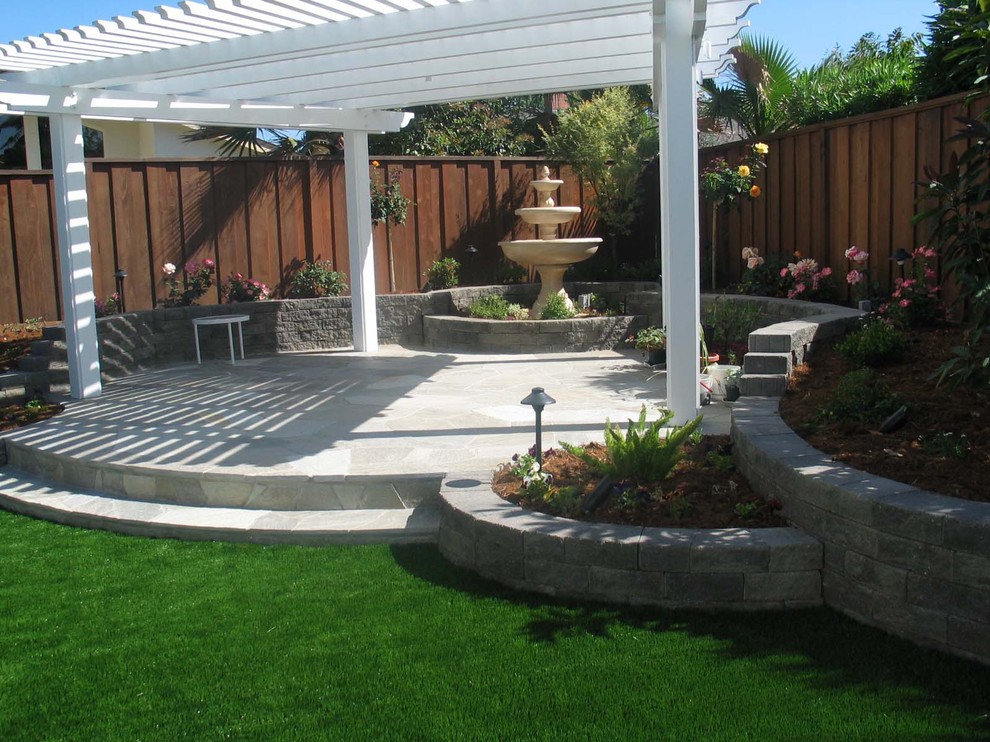 This is an example of a medium sized classic back patio in San Francisco with a water feature, natural stone paving and a pergola.