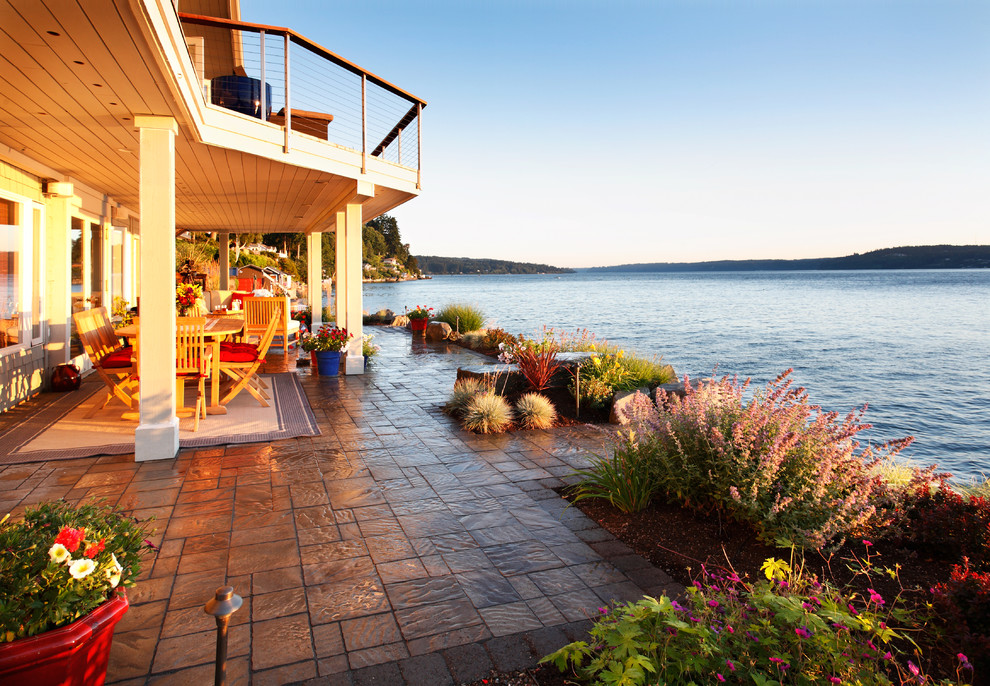 Cette photo montre une terrasse arrière bord de mer avec une cuisine d'été, des pavés en pierre naturelle et un auvent.