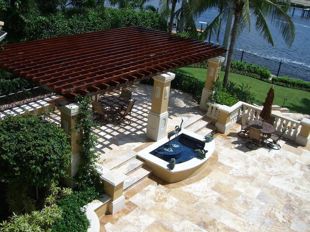 Foto på en stor tropisk uteplats på baksidan av huset, med en fontän, naturstensplattor och en pergola