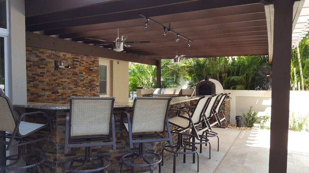 Example of a large tuscan courtyard stone patio kitchen design in Miami with a pergola