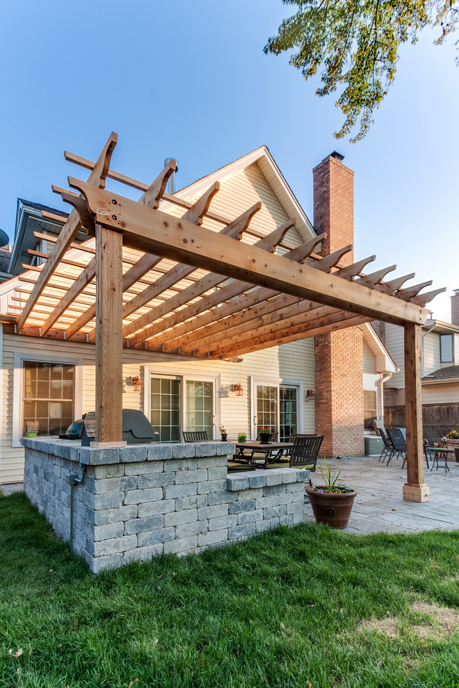 This is an example of a traditional back patio in Chicago with an outdoor kitchen and a pergola.
