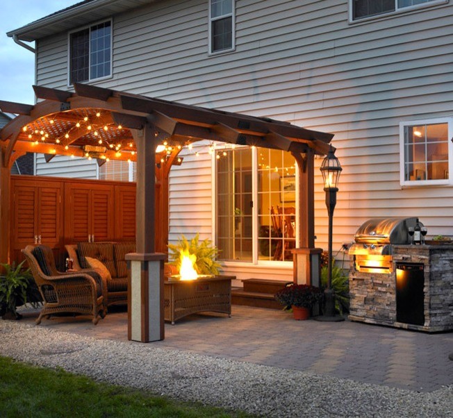 Imagen de patio clásico de tamaño medio en patio trasero con brasero, adoquines de ladrillo y pérgola