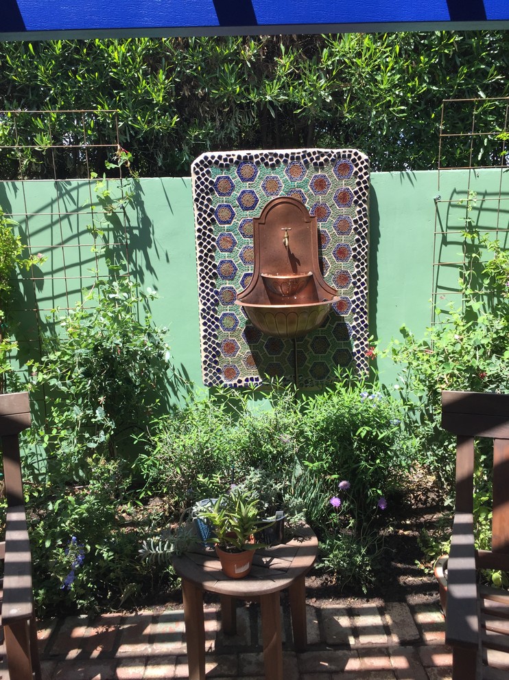 Diseño de patio bohemio pequeño en patio trasero con fuente, adoquines de ladrillo y pérgola