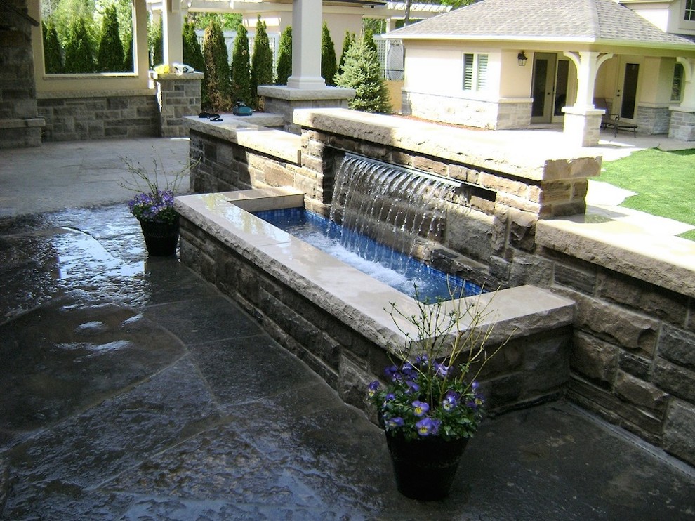 Photo of a classic back patio in Chicago with a water feature, natural stone paving and a roof extension.