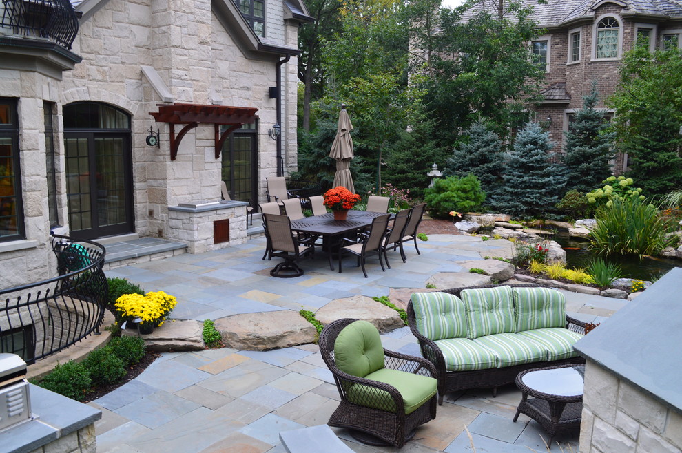 Design ideas for a large rustic back patio in Chicago with an outdoor kitchen, natural stone paving and no cover.