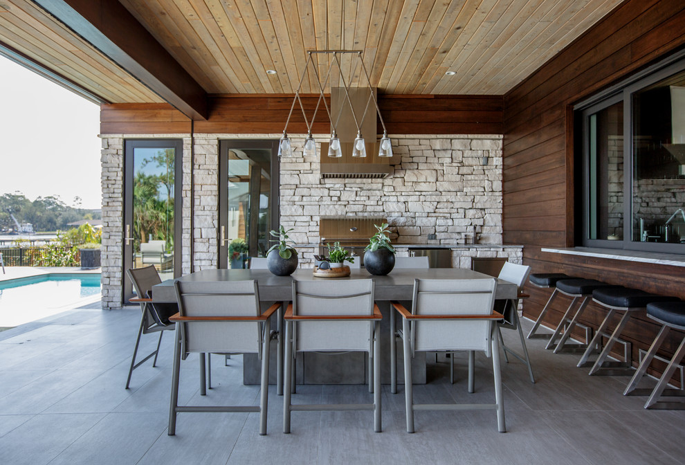 На фото: двор на заднем дворе в современном стиле с летней кухней, покрытием из плитки и навесом с