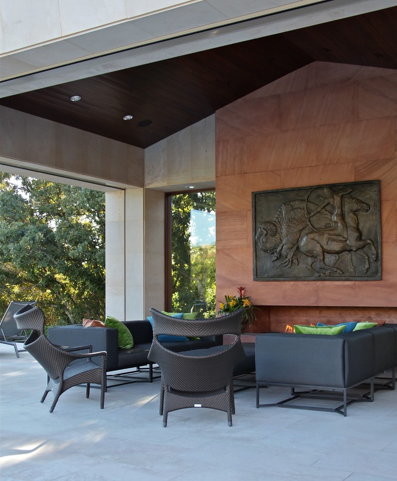 Réalisation d'une grande terrasse arrière design avec un foyer extérieur, des pavés en béton et une extension de toiture.