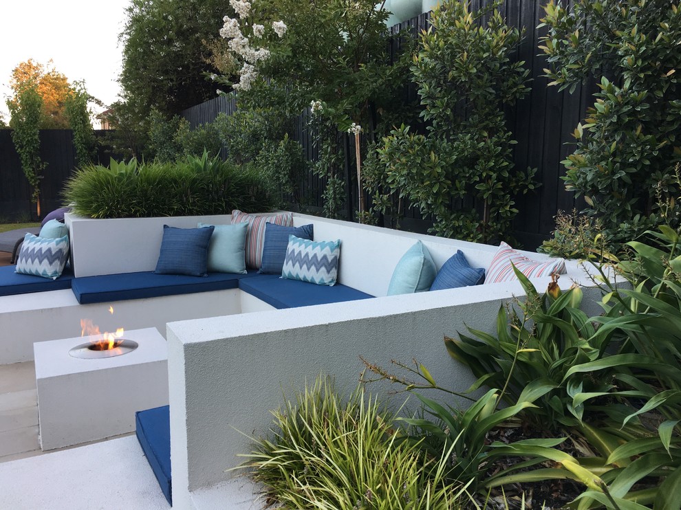 Cette image montre une grande terrasse arrière minimaliste avec un foyer extérieur et des pavés en béton.