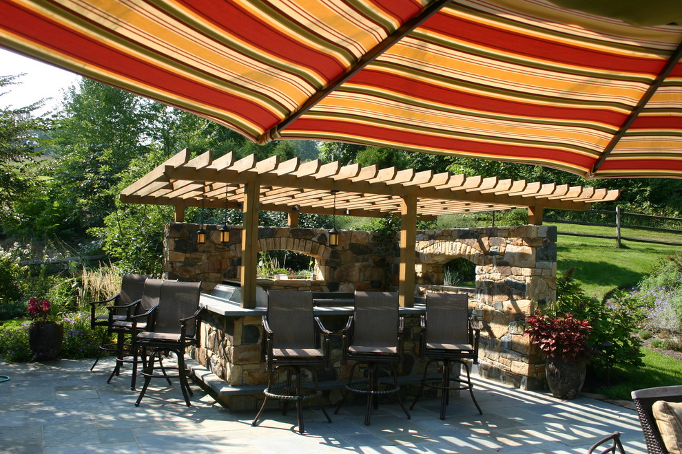 Cette image montre une grande terrasse arrière traditionnelle avec une cuisine d'été, des pavés en pierre naturelle et une pergola.