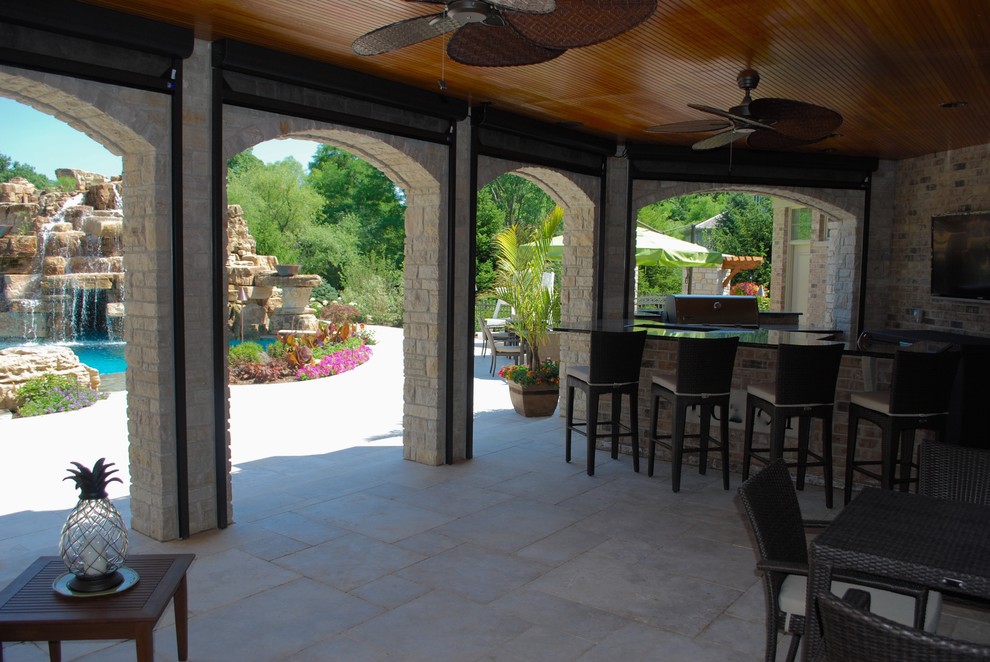 Cette image montre une grande terrasse arrière ethnique avec une cuisine d'été, des pavés en pierre naturelle et une extension de toiture.