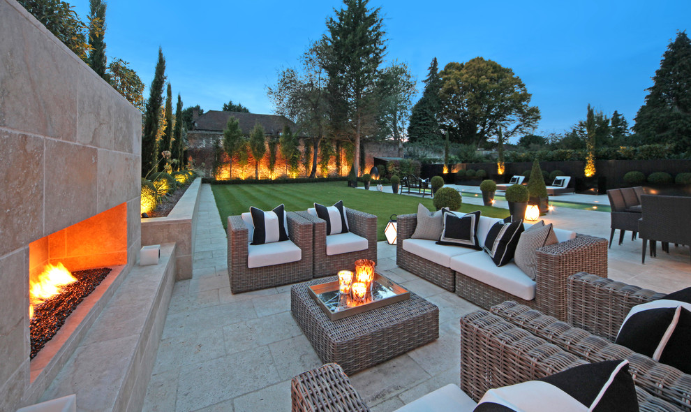 Large contemporary back patio in Surrey with a fire feature, natural stone paving and no cover.